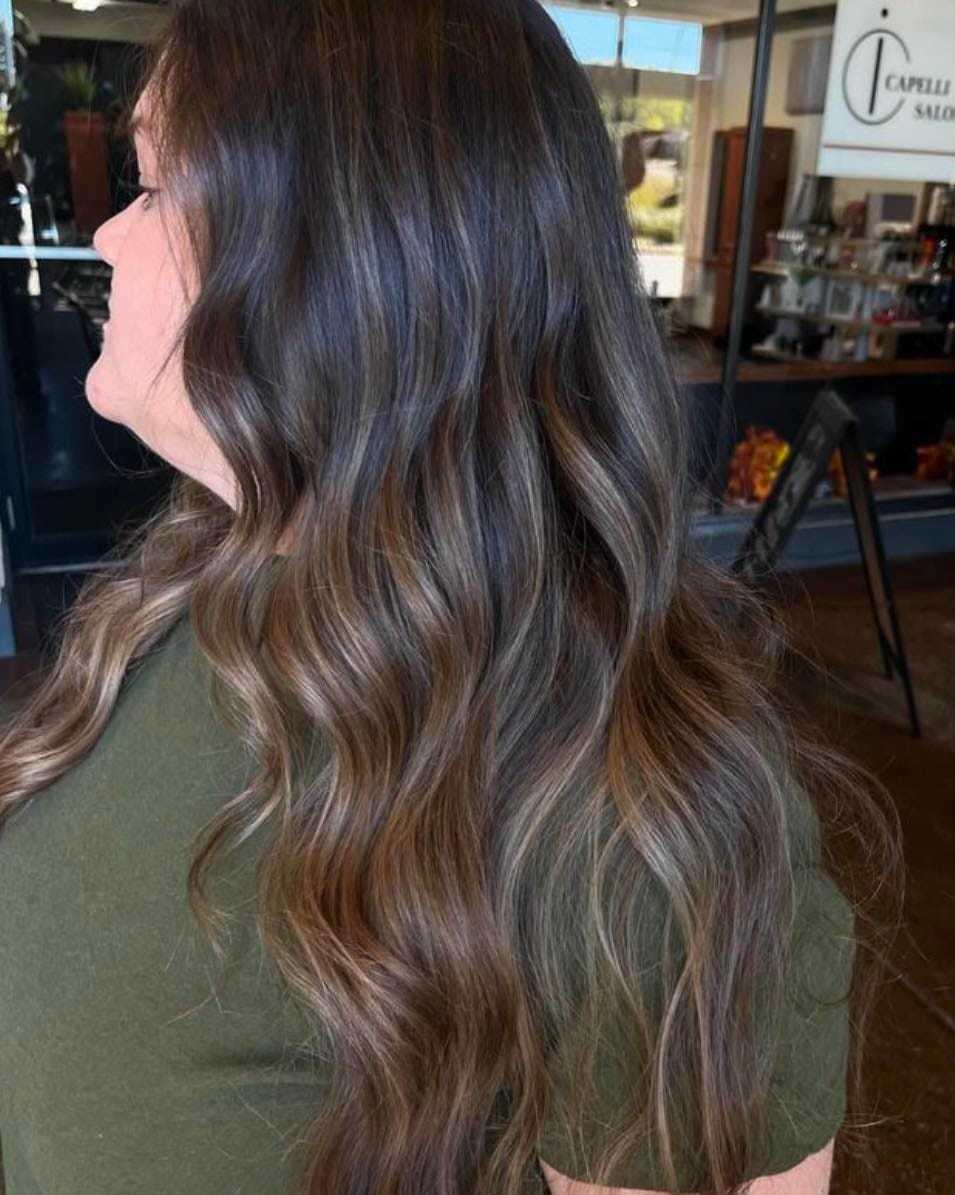 Woman with wavy, highlighted hair in a salon, wearing a green shirt.