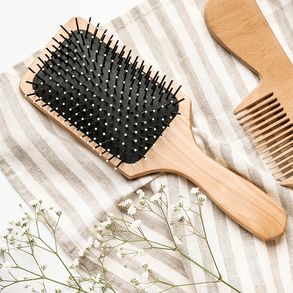 Wooden hairbrush and comb on striped fabric with white flowers.