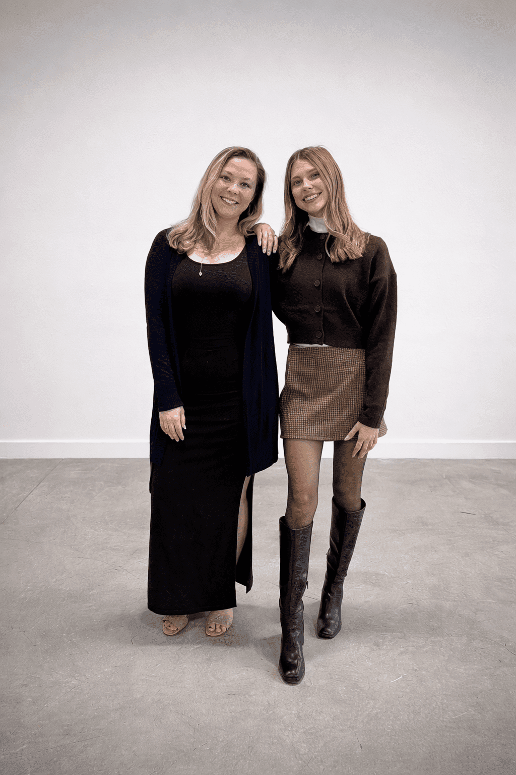 Two women standing and smiling in a minimalist room.