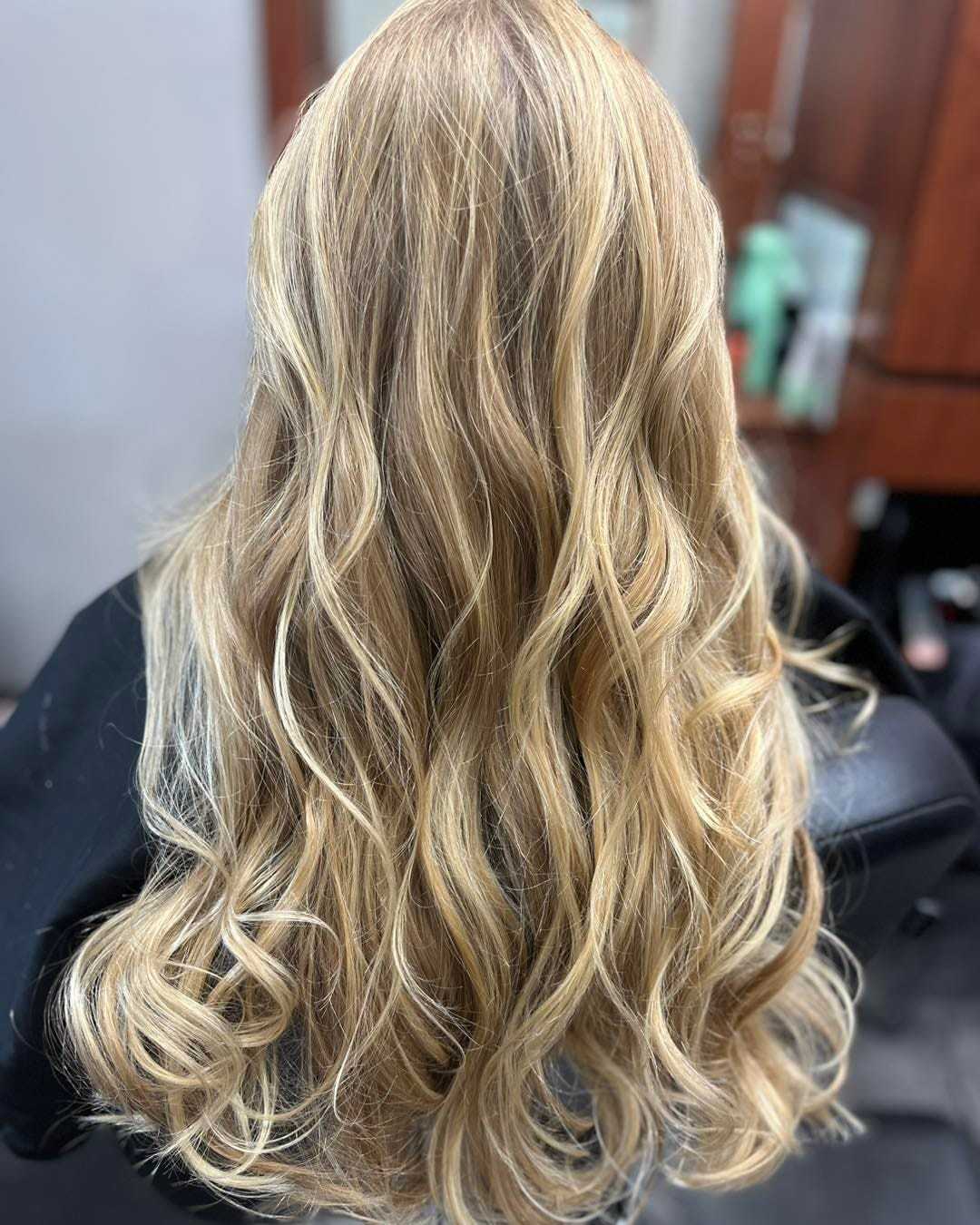 Woman with long, wavy blonde hair sitting in a salon chair.