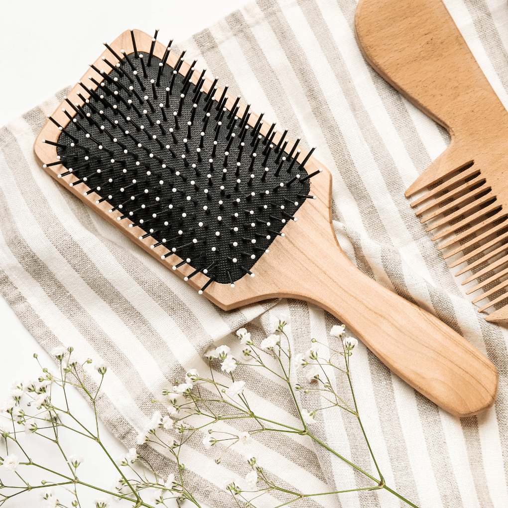 Wooden hairbrush and comb on striped fabric with white flowers.